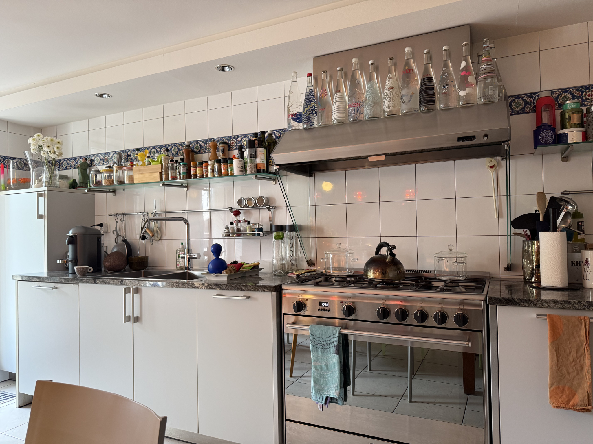Cuisine moderne et équipée avec des rangements, des ustensiles et des bouteilles en verre.