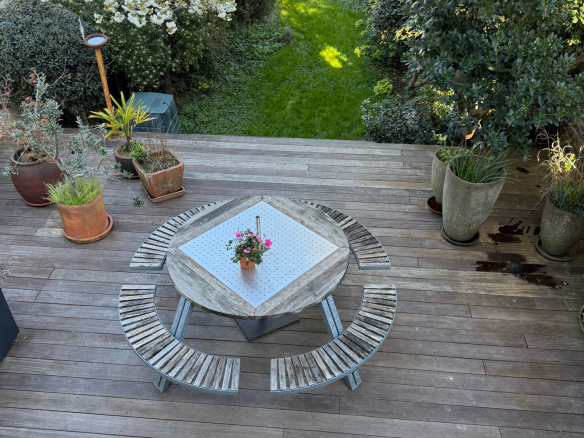 Terrasse en bois avec table et bancs, vue sur jardin verdoyant.