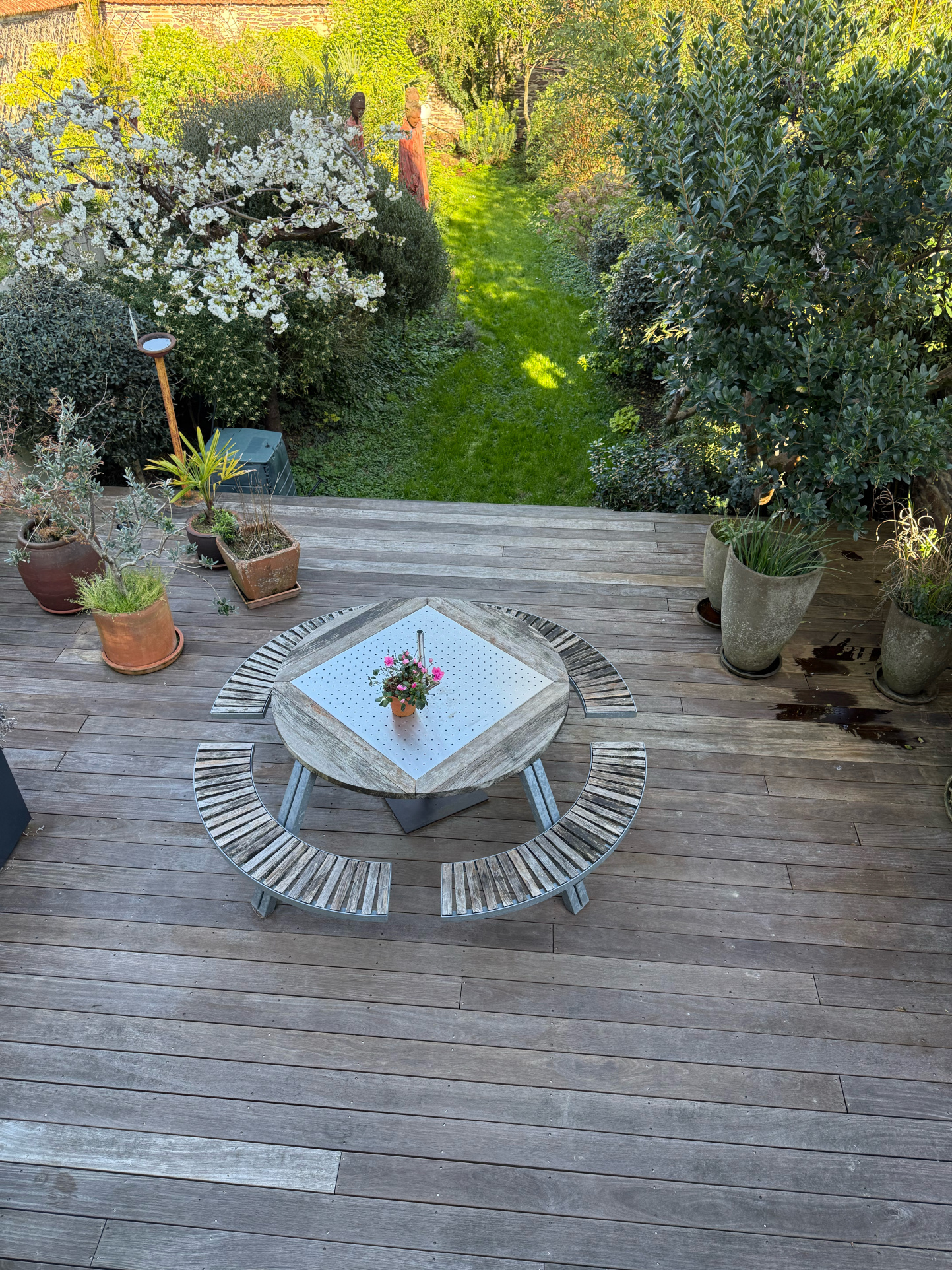 Terrasse en bois avec table et bancs, vue sur jardin verdoyant.