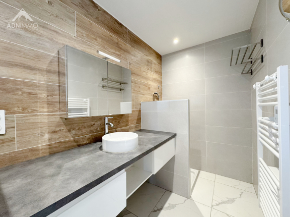 Salle de bain moderne avec meuble vasque et douche, carrelage gris et bois.