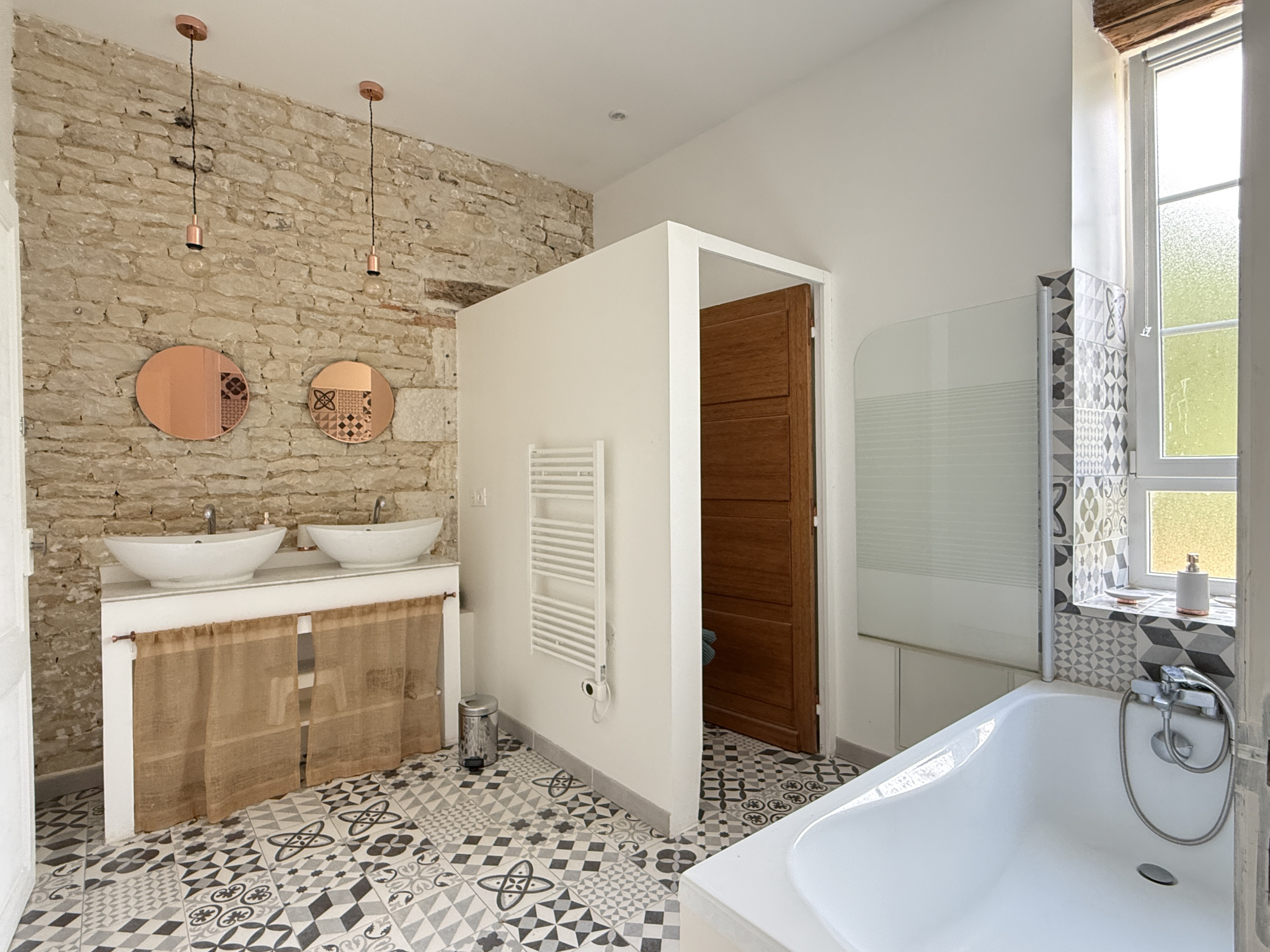 Salle de bain moderne avec murs en pierre et carrelage décoratif, deux lavabos et baignoire.