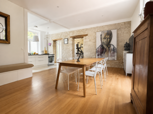 Intérieur d'une maison de caractère avec une grande table en bois et des chaises blanches, murs en pierre apparente.