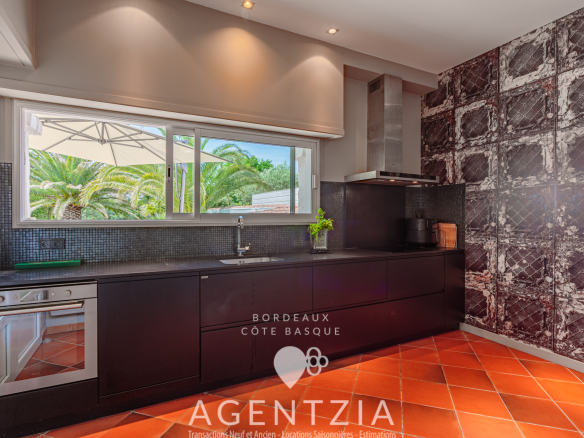 Cuisine moderne d'un appartement de prestige à Bidart, avec vue sur le jardin et des éléments en noir et rouge.