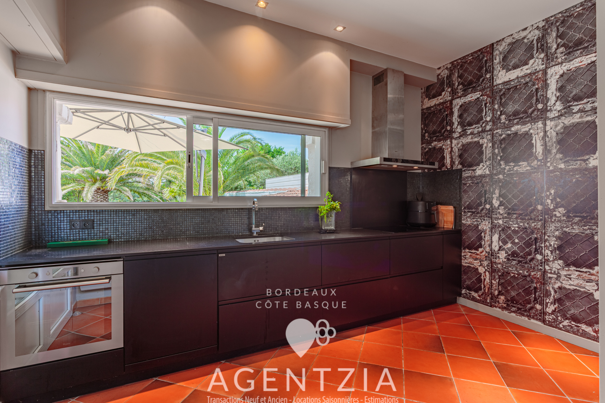 Cuisine d’un appartement de luxe à Bidart Cuisine moderne d'un appartement de prestige à Bidart, avec vue sur le jardin et des éléments en noir et rouge.