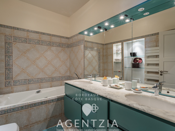 Salle de bain moderne avec baignoire, lavabo et miroir éclairé dans un appartement à Bidart.