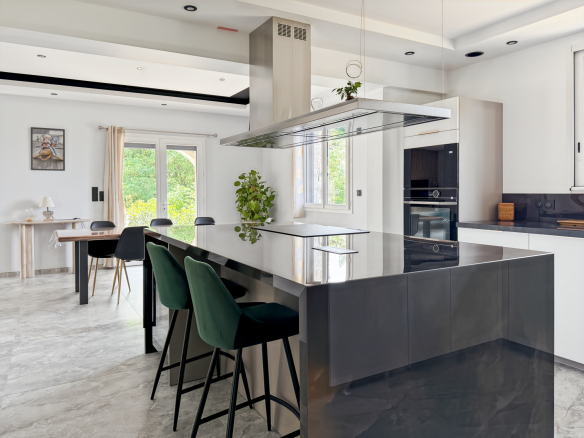 Cuisine moderne avec un îlot central et des chaises noires, ouverte sur un espace lumineux.