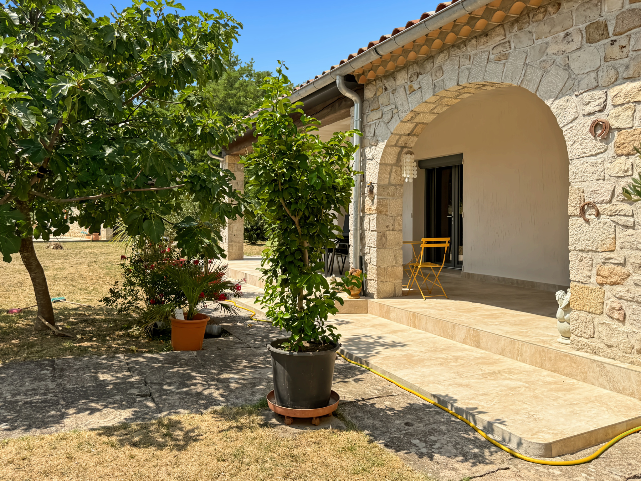Entrée d'une maison en pierre rénovée avec un jardin et des plantes.