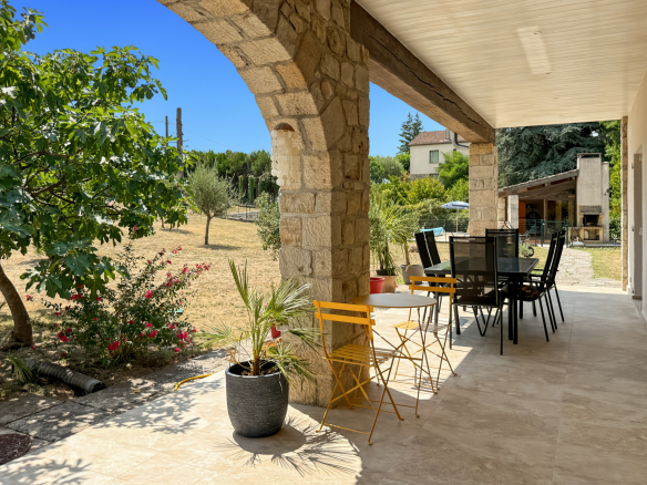 Terrasse d'une maison en pierre rénovée avec mobilier de jardin à Joyeuse, vue sur un terrain arboré.