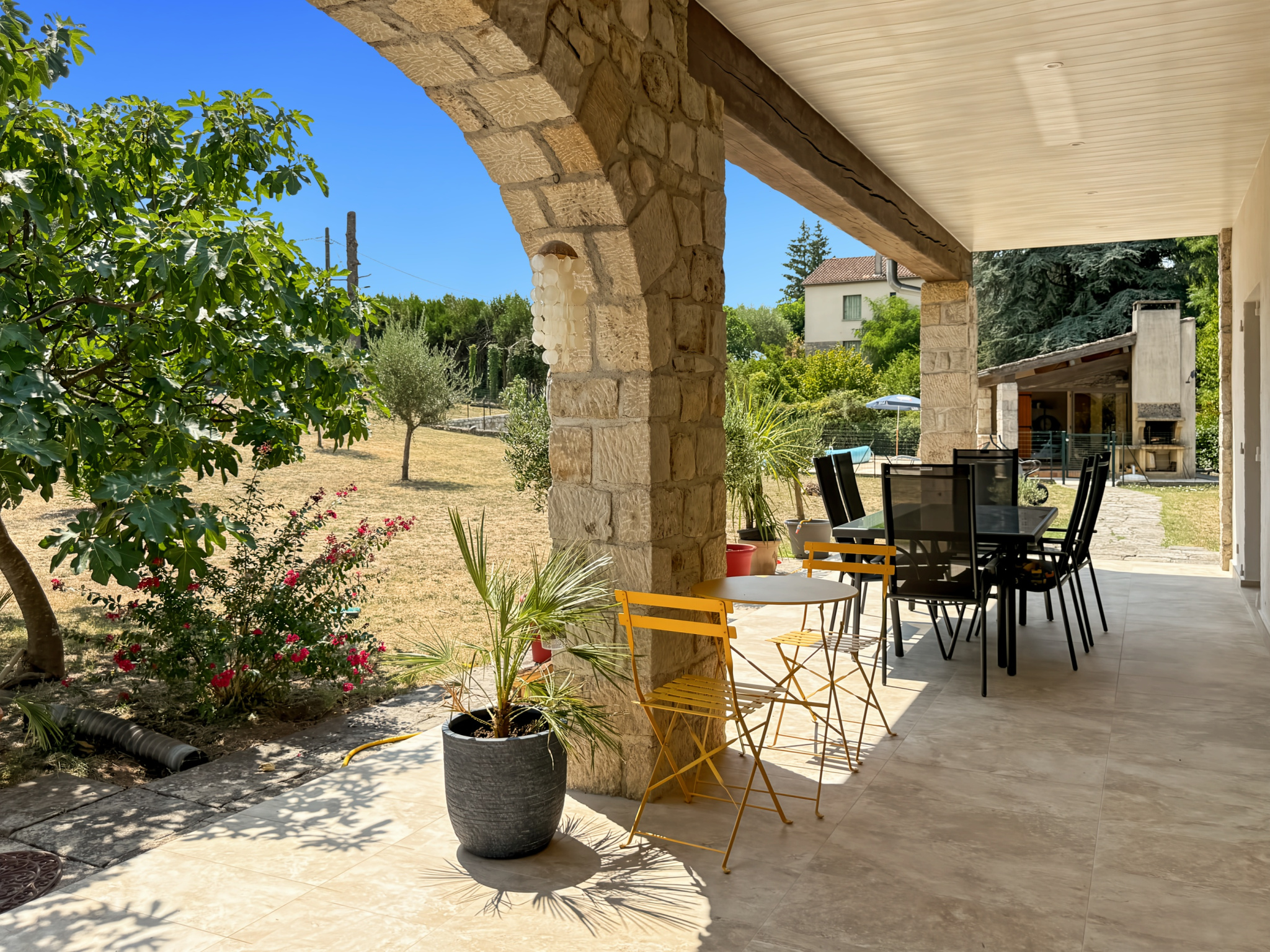 Terrasse d'une maison en pierre rénovée avec mobilier de jardin à Joyeuse, vue sur un terrain arboré.