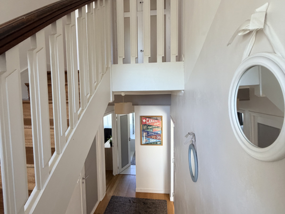 Vue intérieure d'une maison rénovée avec un escalier et un couloir lumineux.