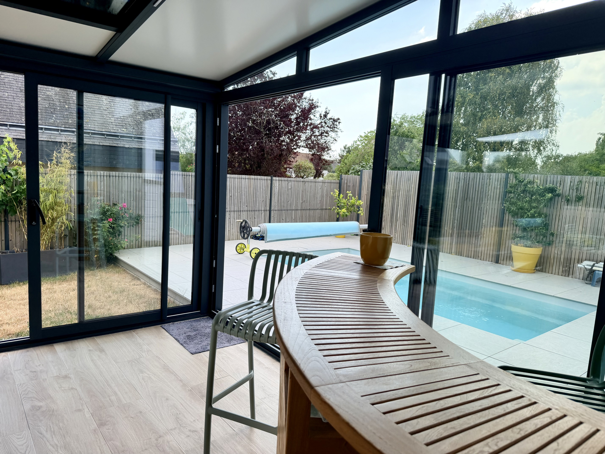 Intérieur d'une véranda moderne avec vue sur un jardin et une piscine.