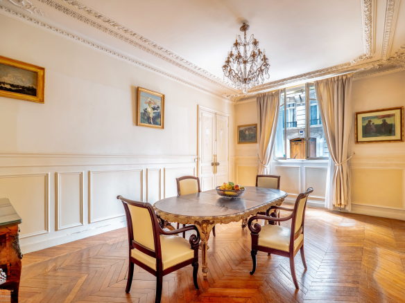 Interior of an elegant garden-level apartment in Paris with a round table and chairs, decorated with paintings.