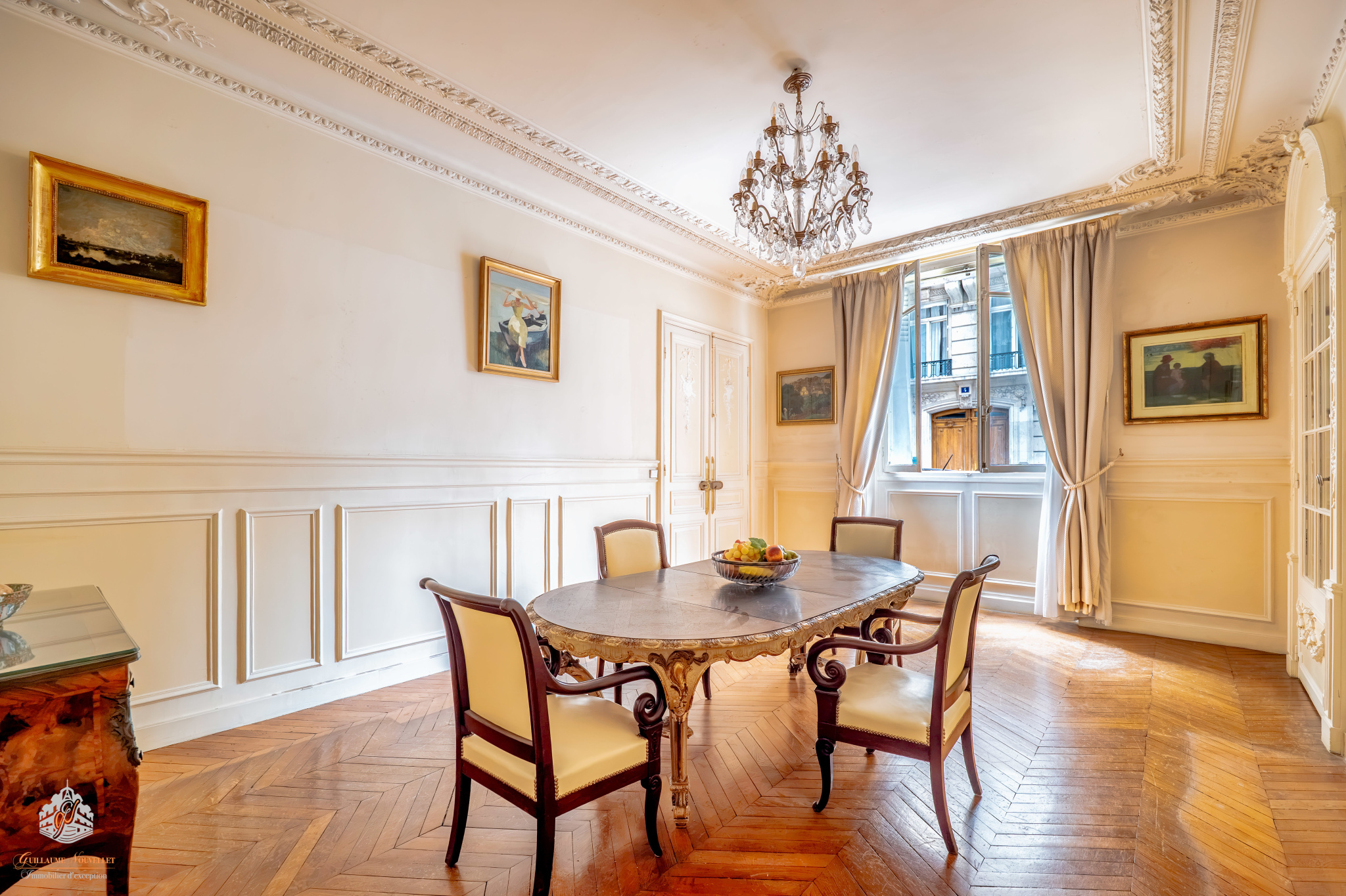 Interior of a ground-floor apartment in Paris Interior of an elegant garden-level apartment in Paris with a round table and chairs, decorated with paintings.