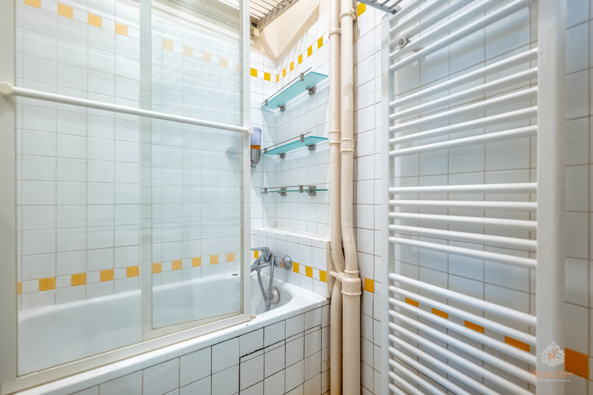 Bathroom in a ground-floor apartment in the 17th arrondissement of Paris Bathroom with bathtub, white tiles and glass elements.