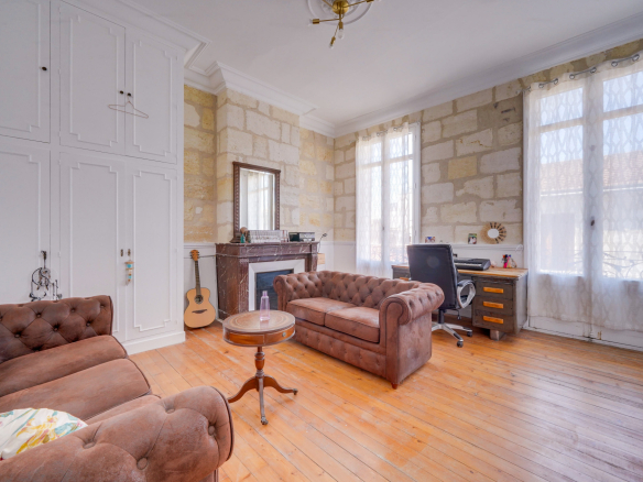 Salon d'une maison bourgeoise à Bordeaux avec canapé en cuir et cheminée en pierre.