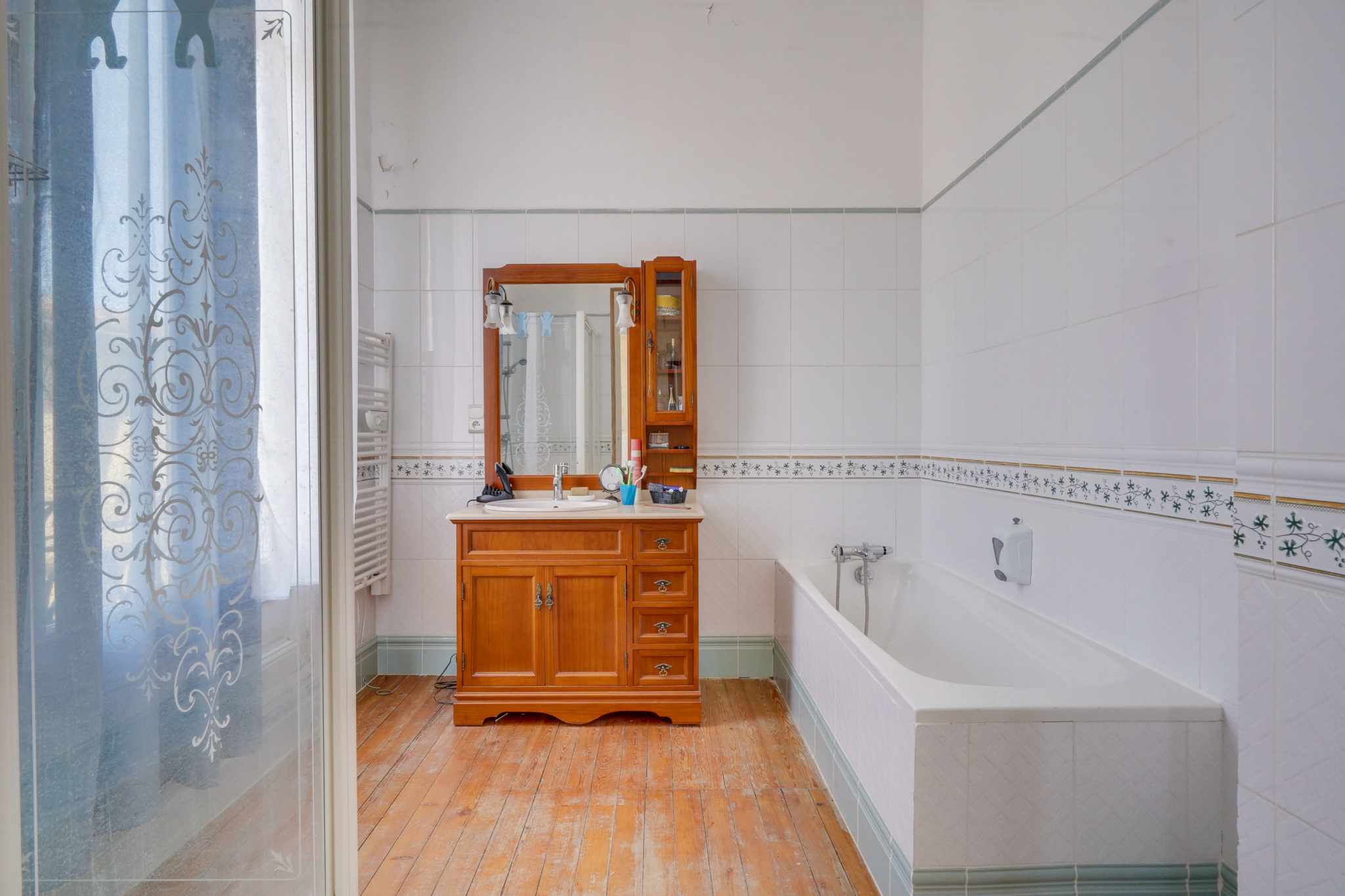 Salle de bain dans une maison bourgeoise à Bordeaux Salle de bain avec baignoire et meuble en bois, carrelage blanc et parquet au sol.