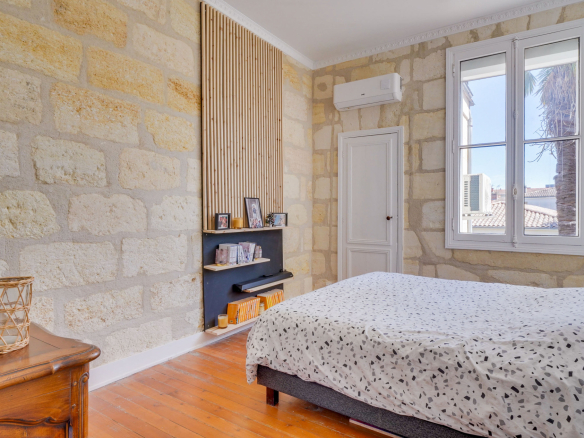 Chambre dans une maison bourgeoise à Bordeaux, avec murs en pierre et fenêtre.