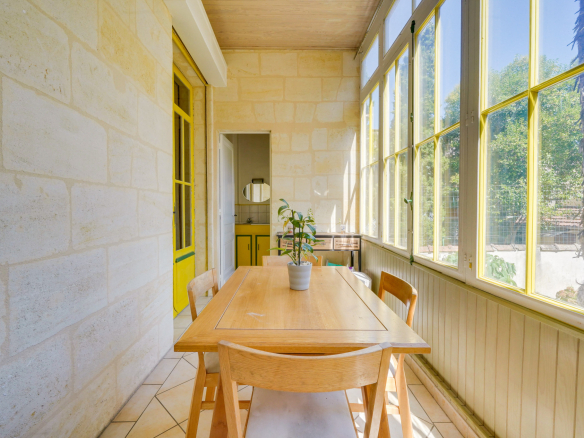 Véranda lumineuse avec table en bois et chaises, maison bourgeoise à Bordeaux.