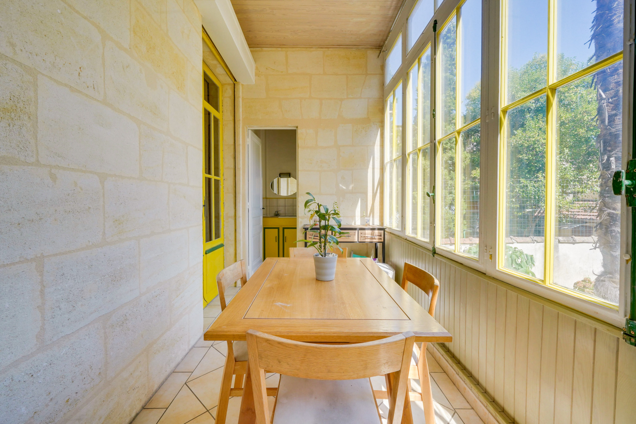 Véranda d’une maison bourgeoise à Bordeaux Véranda lumineuse avec table en bois et chaises, maison bourgeoise à Bordeaux.