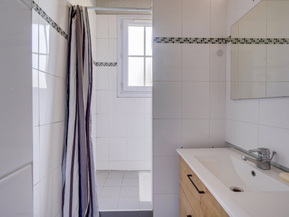 Salle de bain moderne avec douche et lavabo, carrelage blanc et meuble en bois.