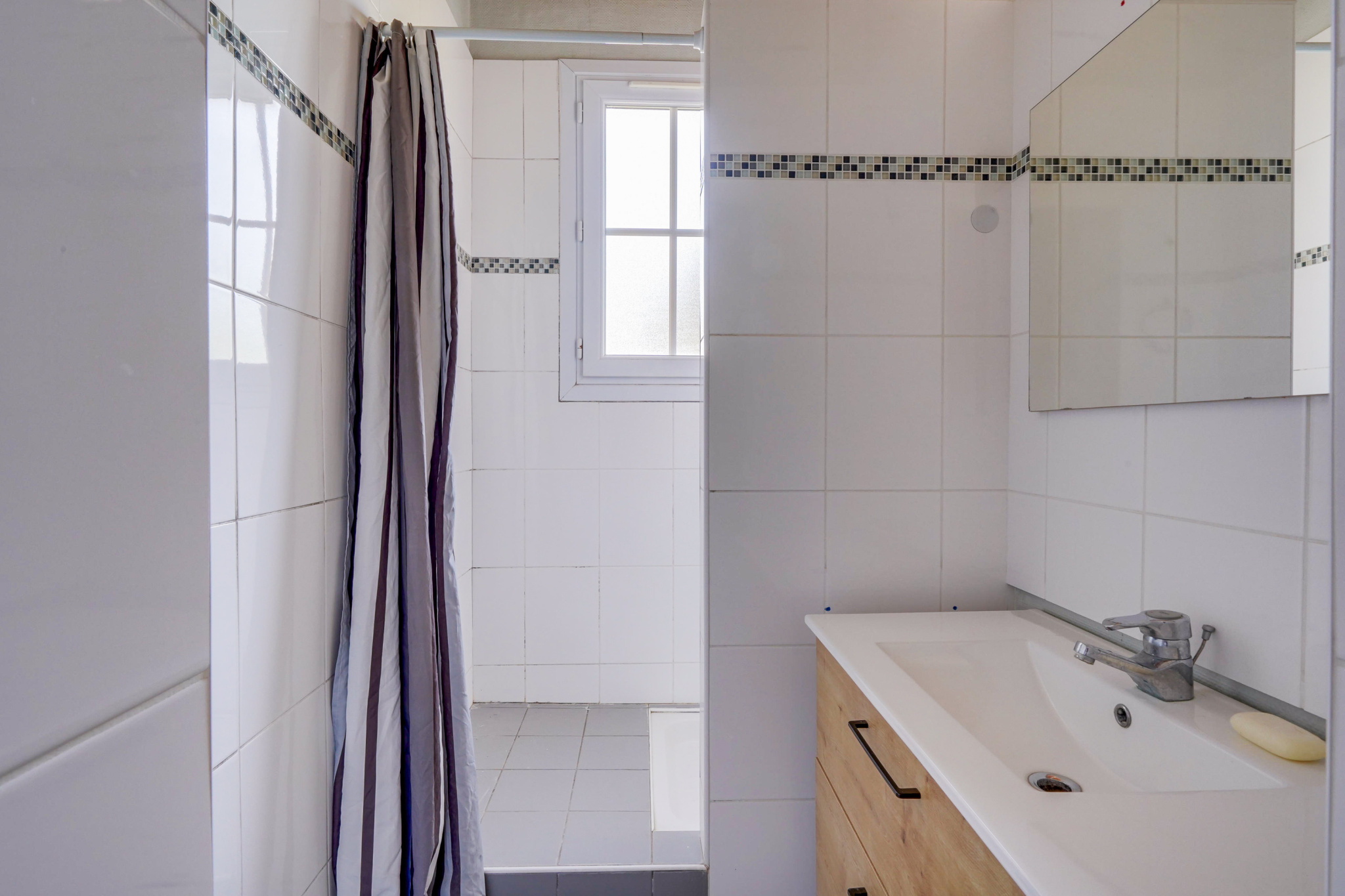 Salle de bain dans une maison à Bordeaux Salle de bain moderne avec douche et lavabo, carrelage blanc et meuble en bois.