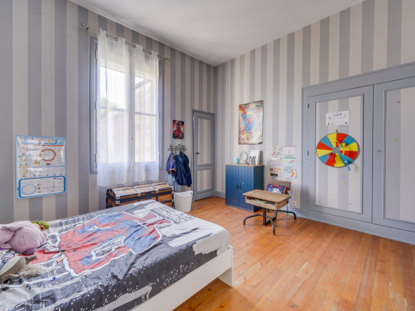 Chambre d'une maison bourgeoise à Bordeaux avec des murs rayés et un lit avec des draps colorés.