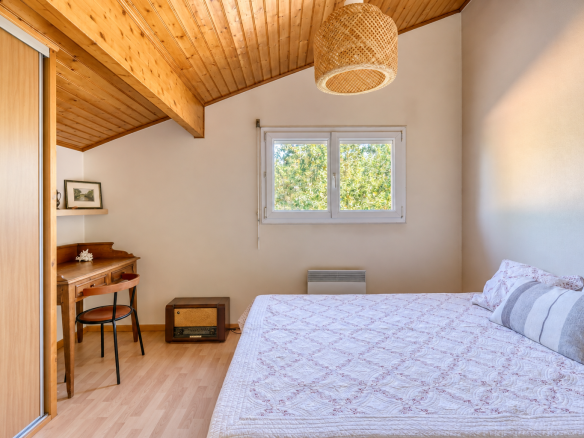 Chambre d'une maison avec lit et bureau, murs clairs et plafond en bois.