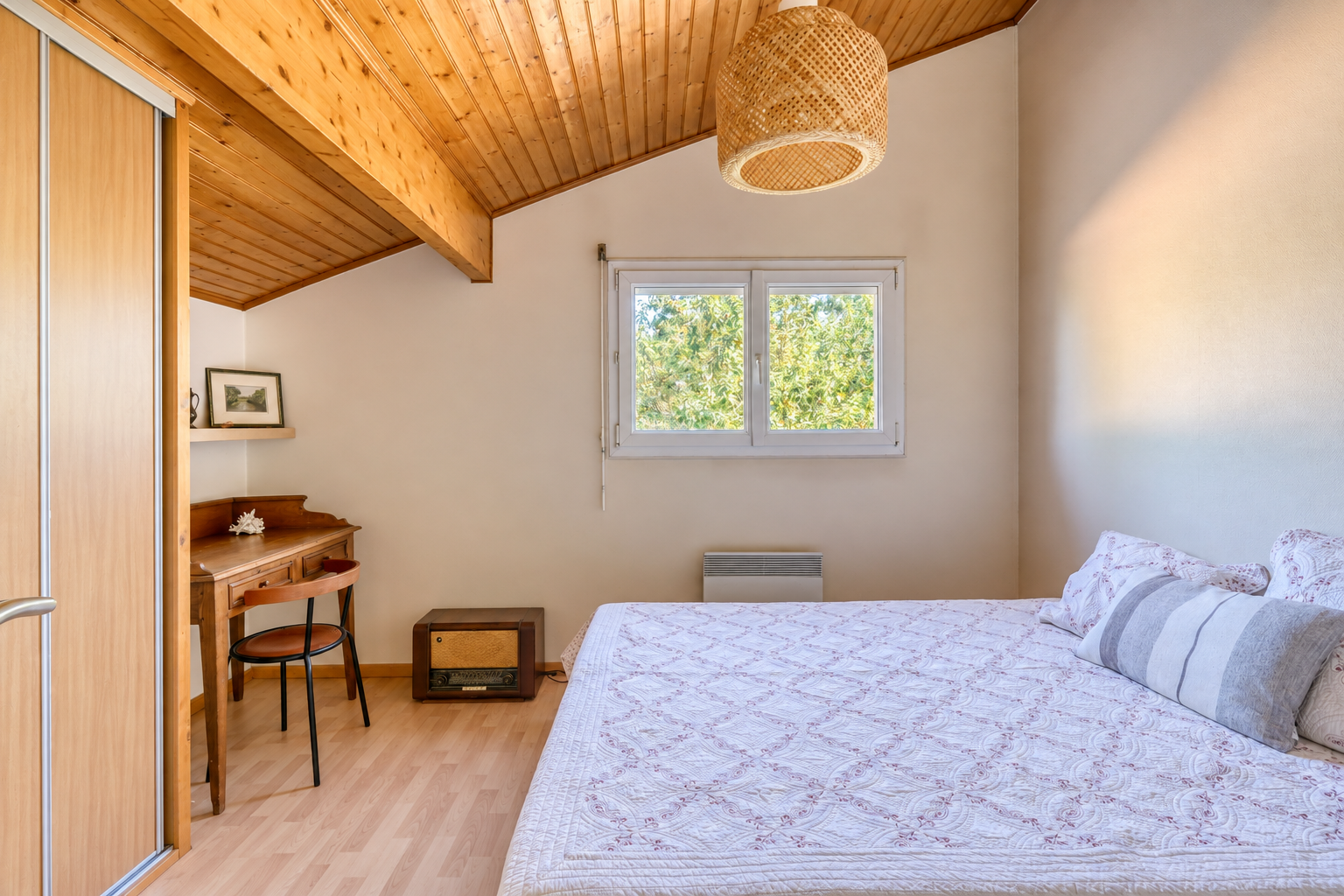 Chambre dans une maison familiale Chambre d'une maison avec lit et bureau, murs clairs et plafond en bois.