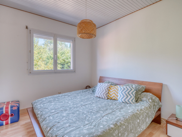 Chambre avec lit double, coussins colorés et fenêtre laissant entrer la lumière.