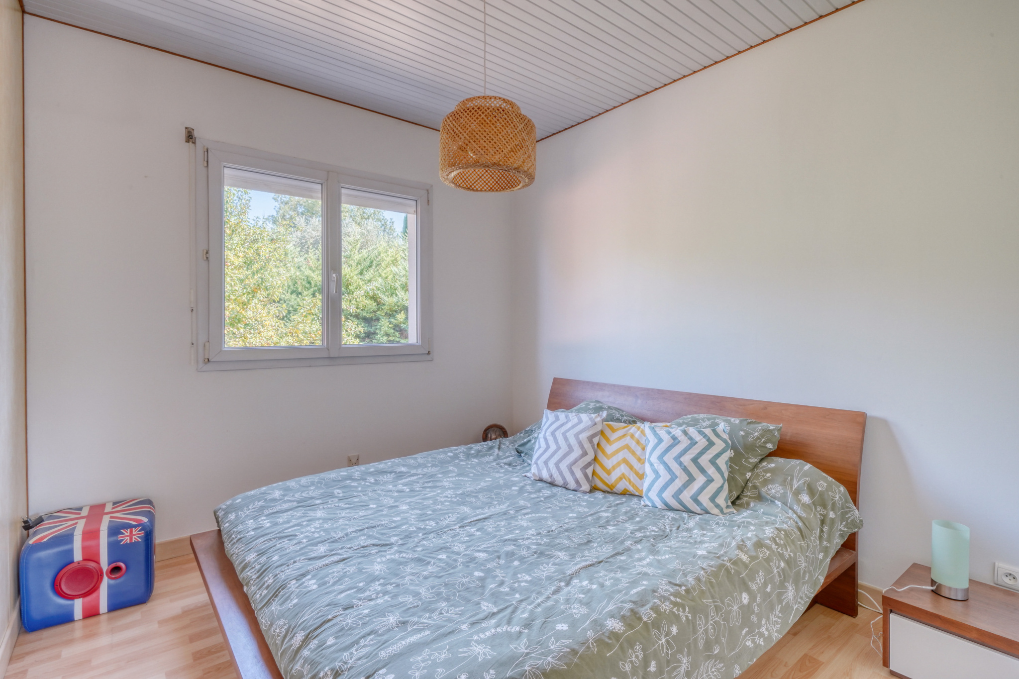 Chambre d’une maison à Montussan Chambre avec lit double, coussins colorés et fenêtre laissant entrer la lumière.