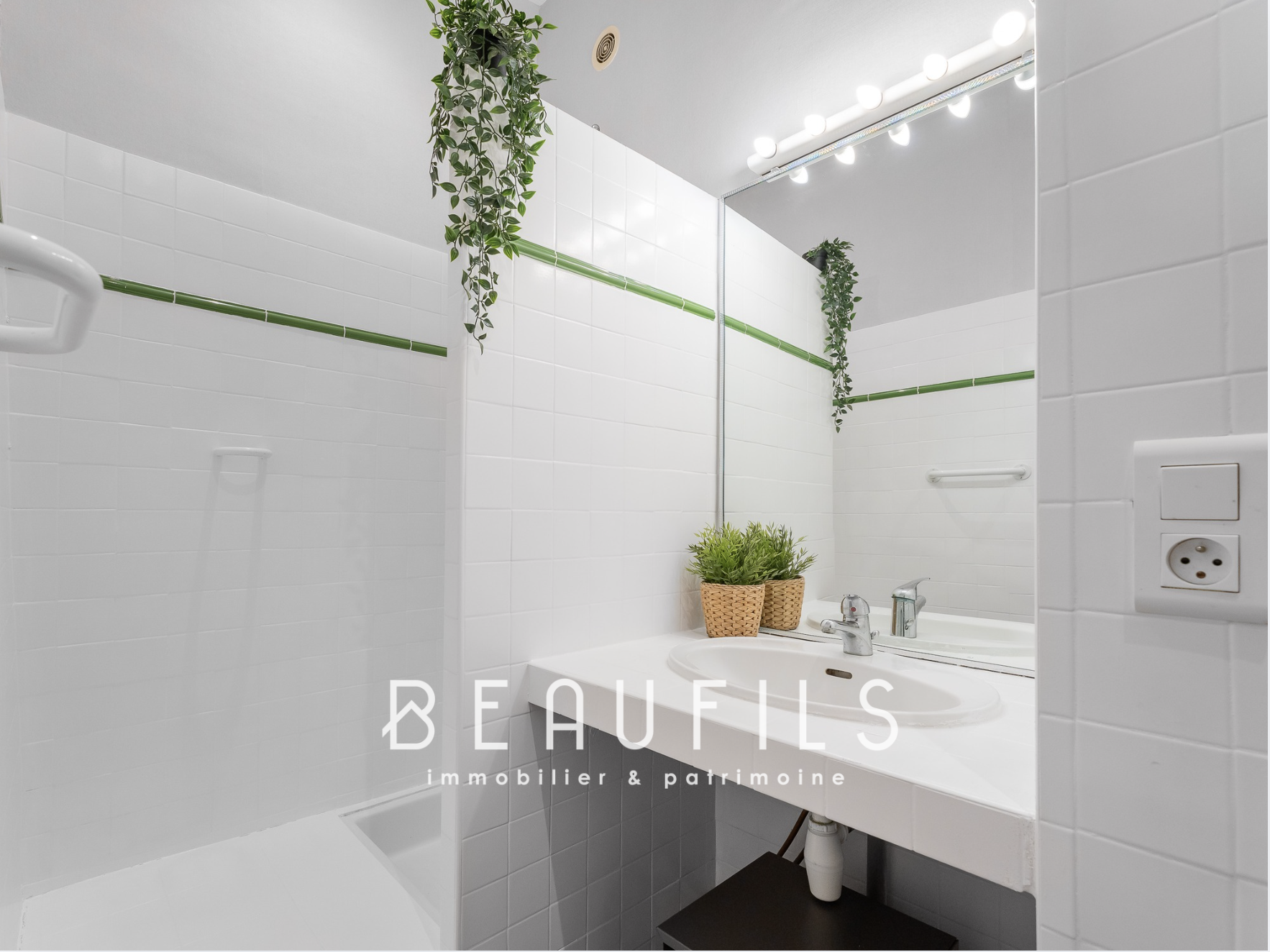 Salle de bain rénovée Salle de bain moderne avec carrelage blanc, miroir lumineux et plante décorative.