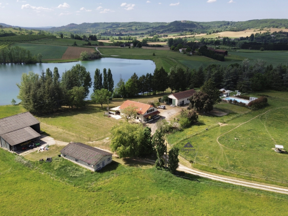 Vue aérienne d'une maison avec 5 chambres, granges et piscine, entourée de prairies et d'un lac à Penne-d'Agenais.