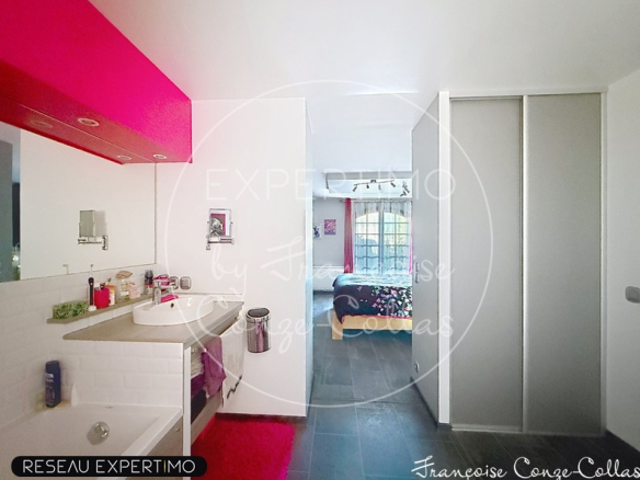 Salle de bain moderne avec lavabo et douche, chambre à coucher visible en arrière-plan.