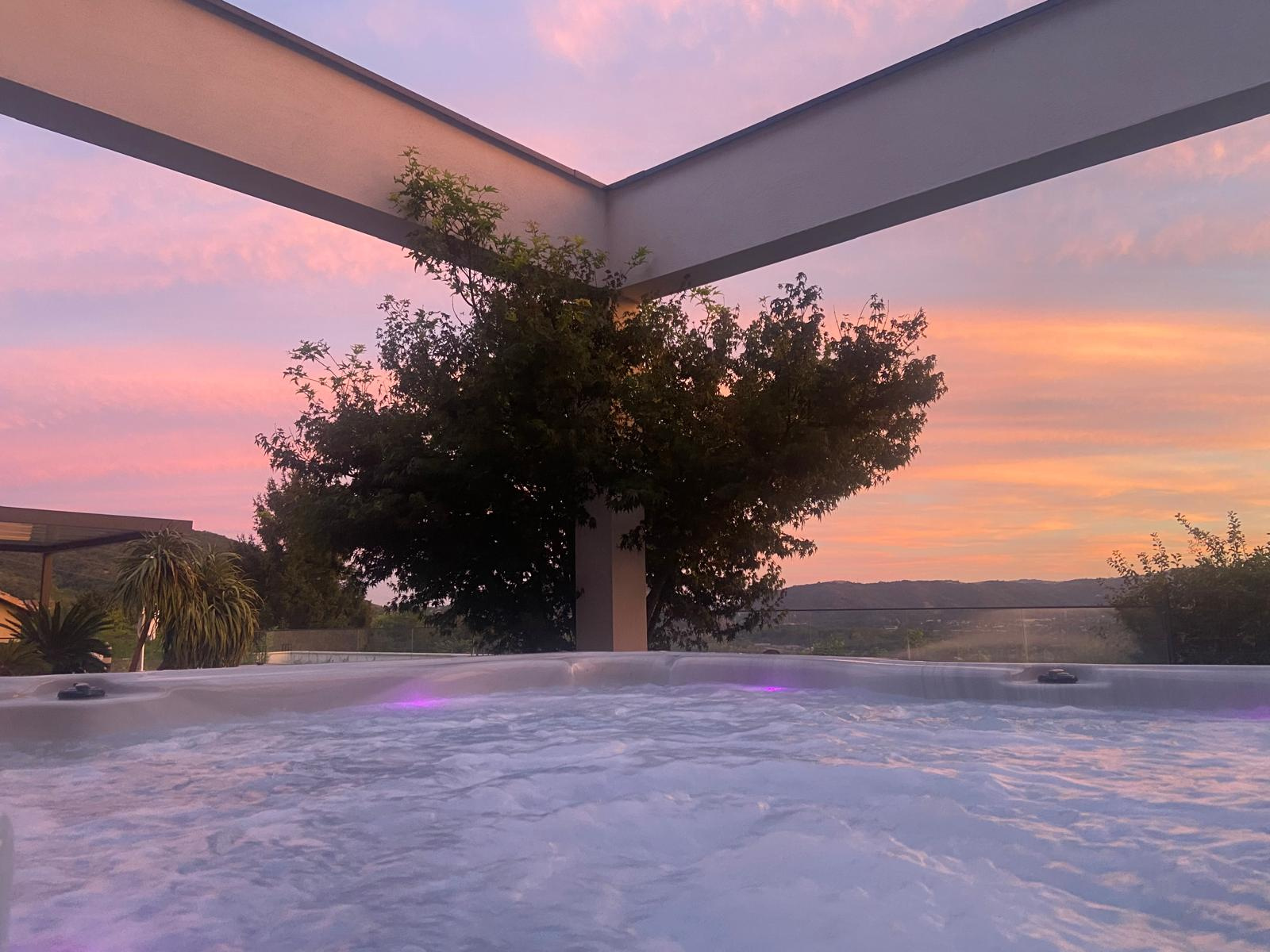 Terrasse avec jacuzzi et vue sur les vignobles Vue depuis une terrasse avec jacuzzi, ciel coloré au coucher du soleil et paysage de vignobles en arrière-plan.