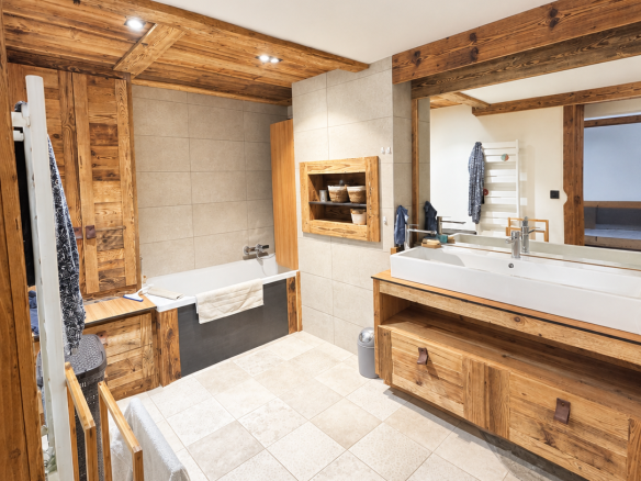 Salle de bain spacieuse avec baignoire et meuble en bois, carrelage clair, miroir et douche.