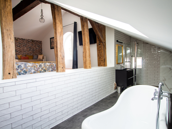 Intérieur d'une maison rénovée avec baignoire, murs en briques et poutres apparentes.