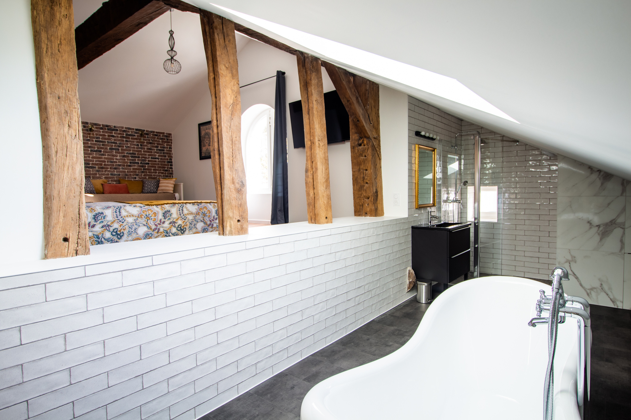 Intérieur d'une maison rénovée avec baignoire, murs en briques et poutres apparentes.