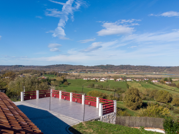 Vue panoramique sur la campagne depuis une terrasse avec balustrade rouge.