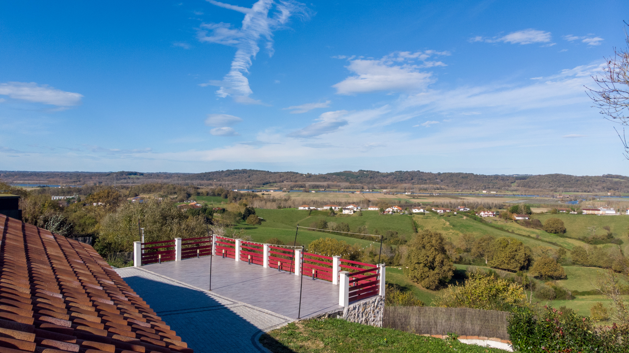 Vue panoramique sur la campagne depuis une terrasse avec balustrade rouge.