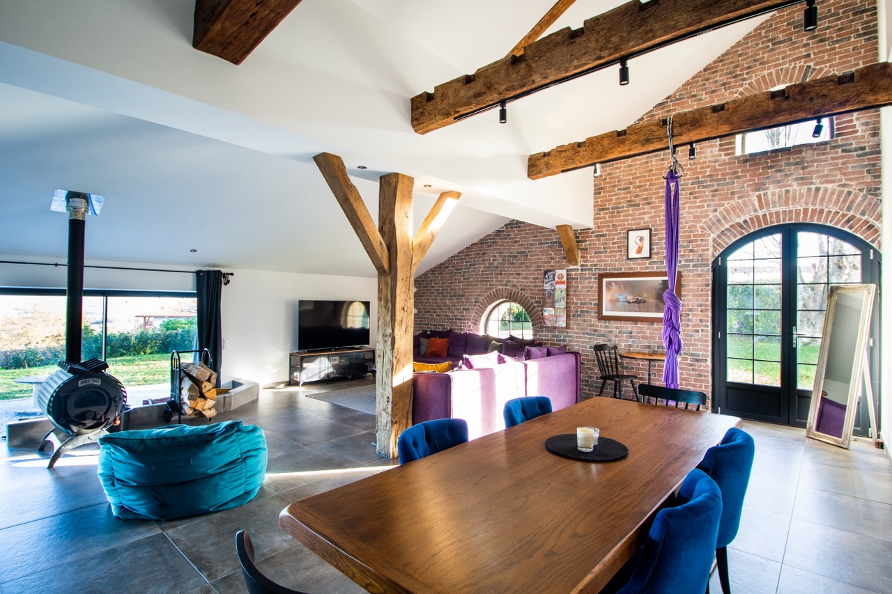 Intérieur d'une maison rénovée avec poutres apparentes, salon lumineux et coin repas.