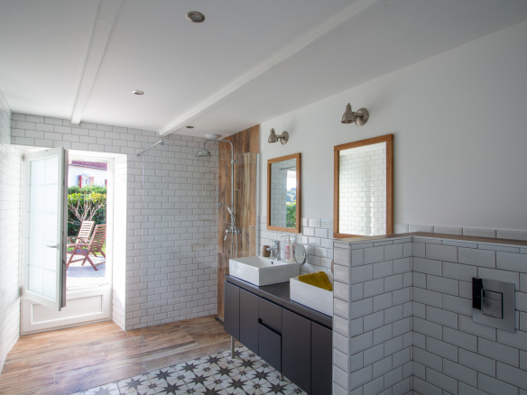 Salle de bain moderne avec carrelage, lavabo et fenêtres ouvertes sur l'extérieur.