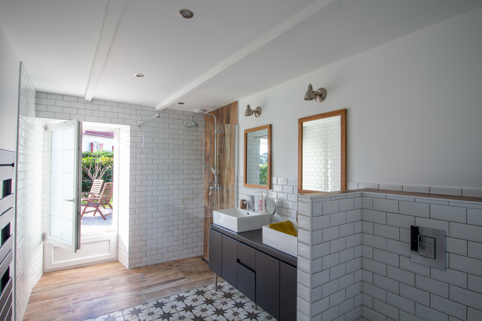 Salle de bain moderne avec carrelage, lavabo et fenêtres ouvertes sur l'extérieur.