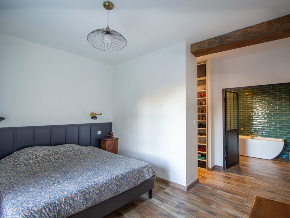 Chambre d'une maison rénovée avec lit, éclairage et salle de bain attenante.