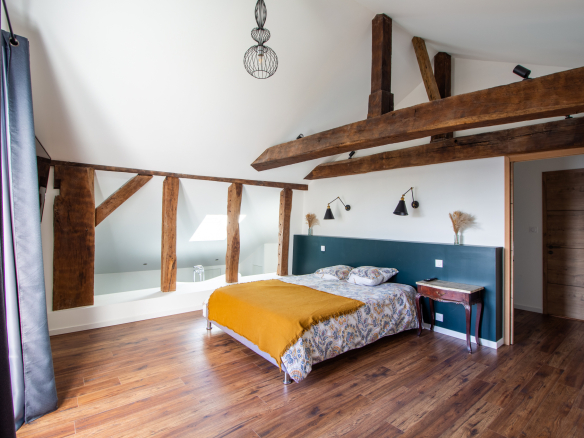 Chambre d'une maison rénovée avec poutres apparentes et lit confortable.