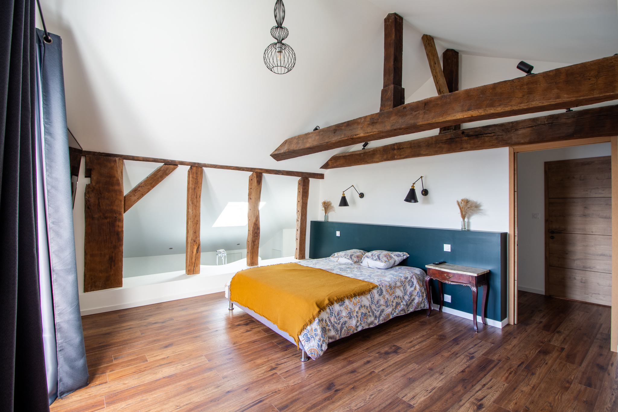 Chambre d'une maison rénovée avec poutres apparentes et lit confortable.
