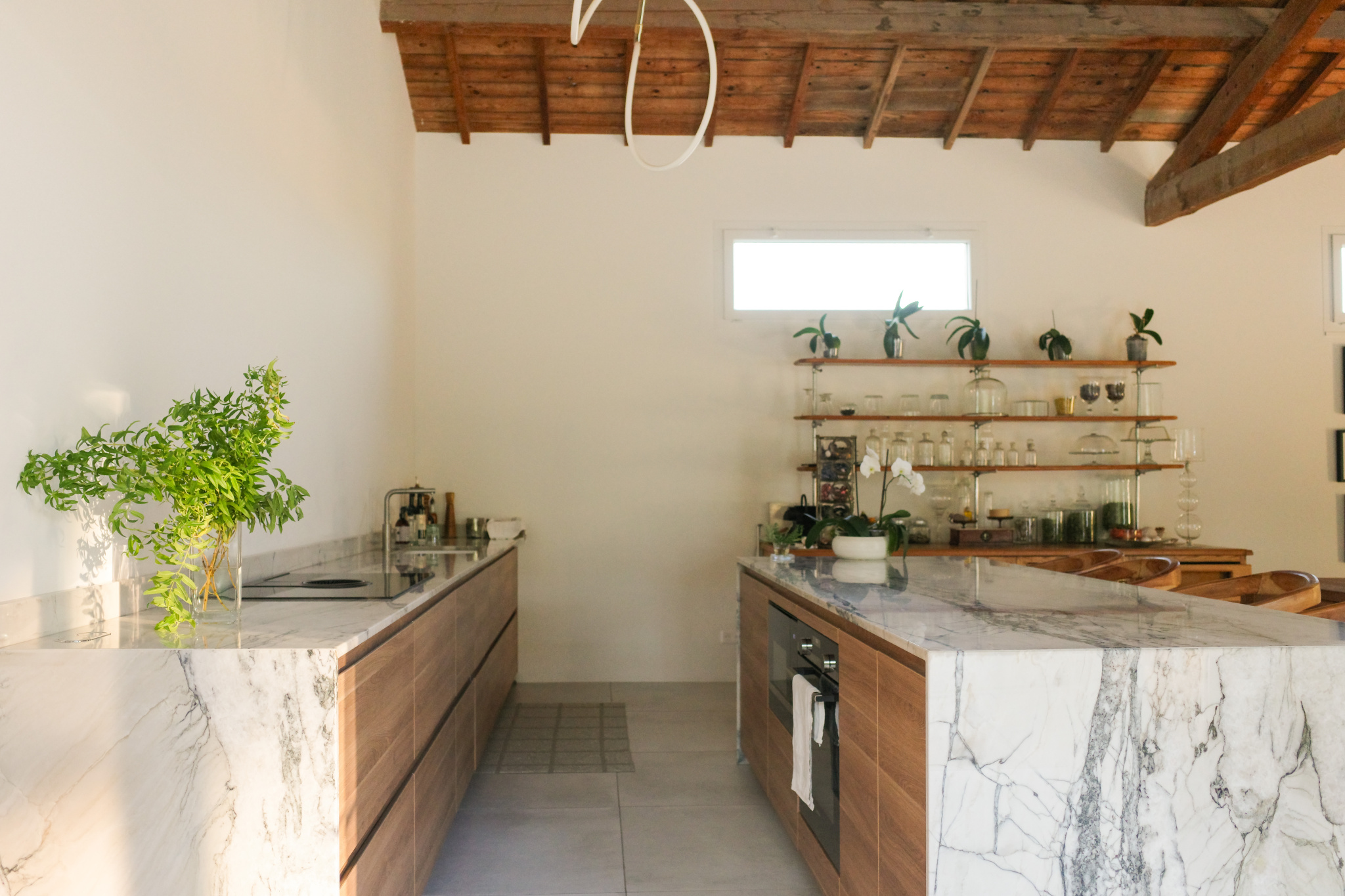 Modern kitchen with central island and marble elements, natural lighting, decorative plants.