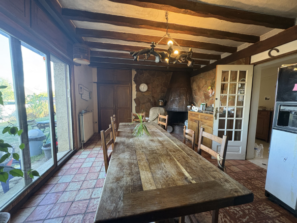 Intérieur d'une maison avec une grande table en bois, des chaises, et un coin cuisine.