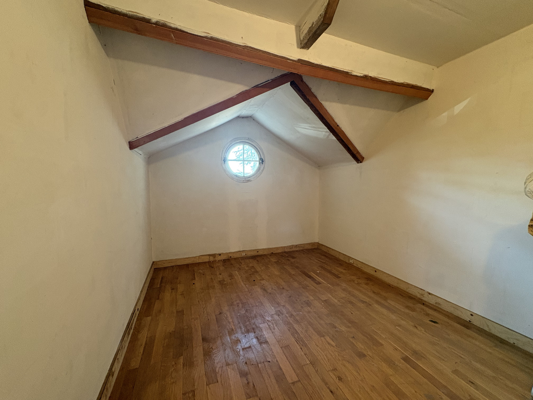 Chambre sous les combles à Roissy-en-Brie Intérieur d'une chambre sous les combles avec un sol en bois et une fenêtre ronde.