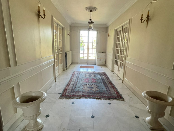 Intérieur d'une maison avec un grand hall d'entrée, sol en marbre et tapis au centre.