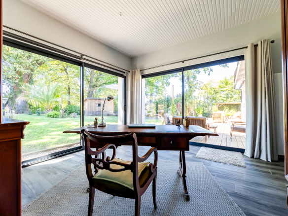 Intérieur d'une maison de plain pied avec un bureau et de grandes fenêtres donnant sur le jardin.